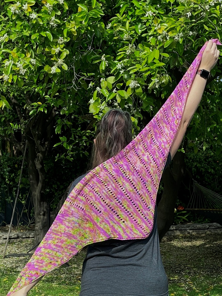 A knit shawl in pink, green, and yellow, being held at a diagonal 