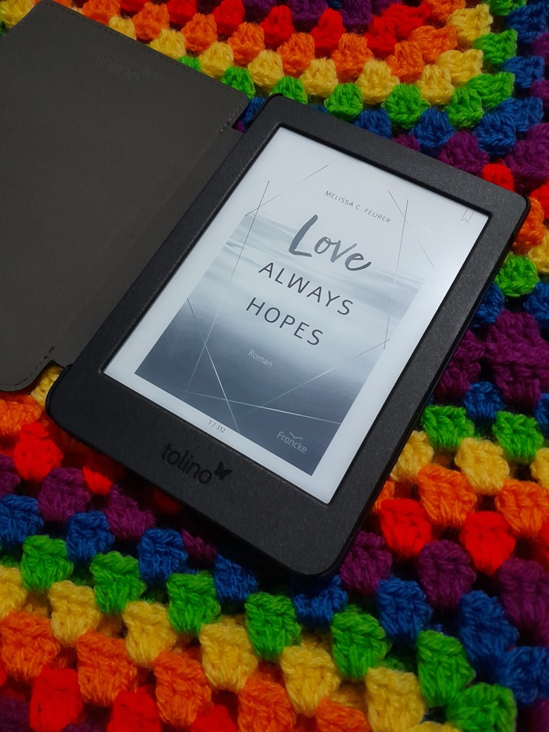 Das Cover von "Love Always Hopes" (Melissa C. Feurer) auf einem E-Reader vor einem bunten Hintergrund